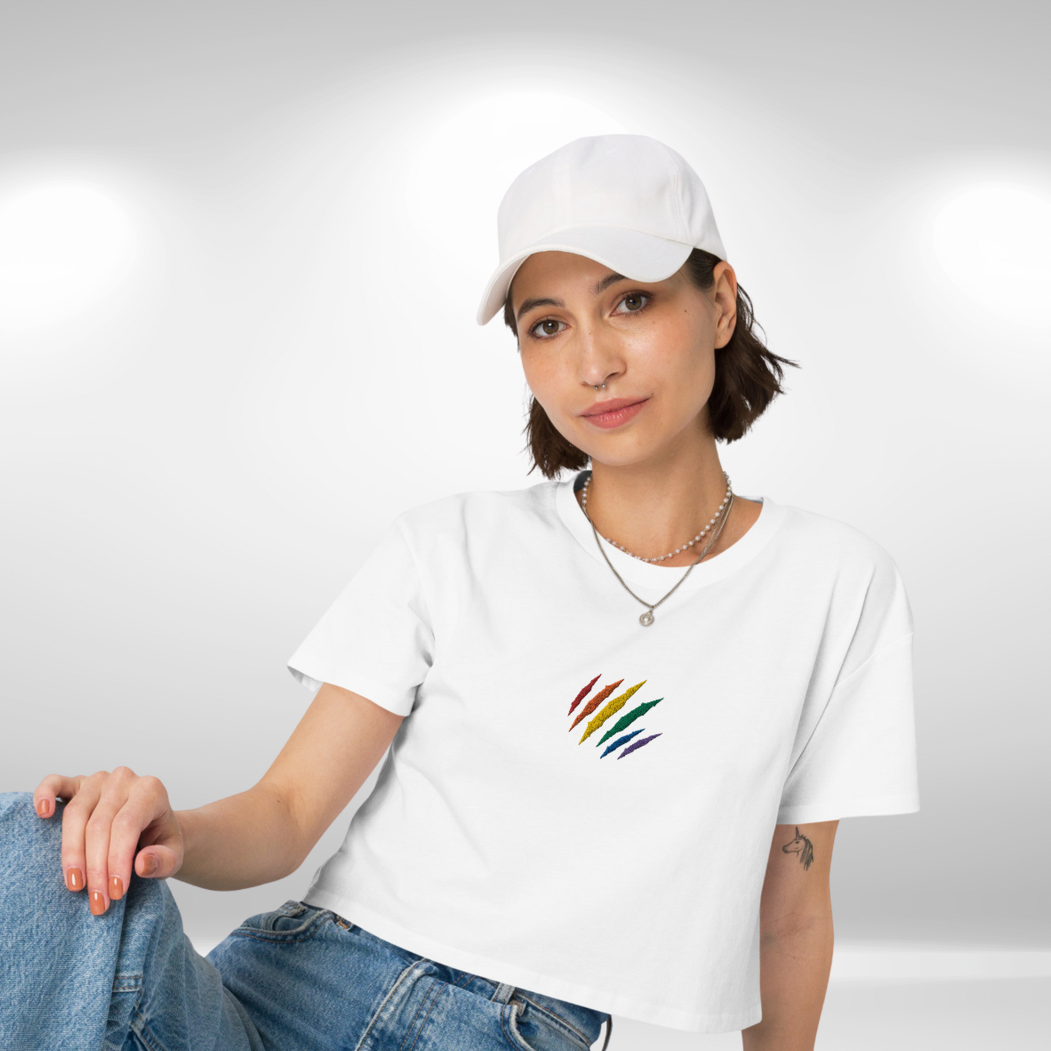 Female model wearing a white crop top featuring an embroidered lion mark in the colors of the rainbow