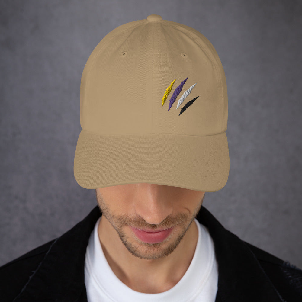 A male model wearing out khaki baseball hat featuring non-binary pride scratch mark embroidery with a low profile, adjustable strap.
