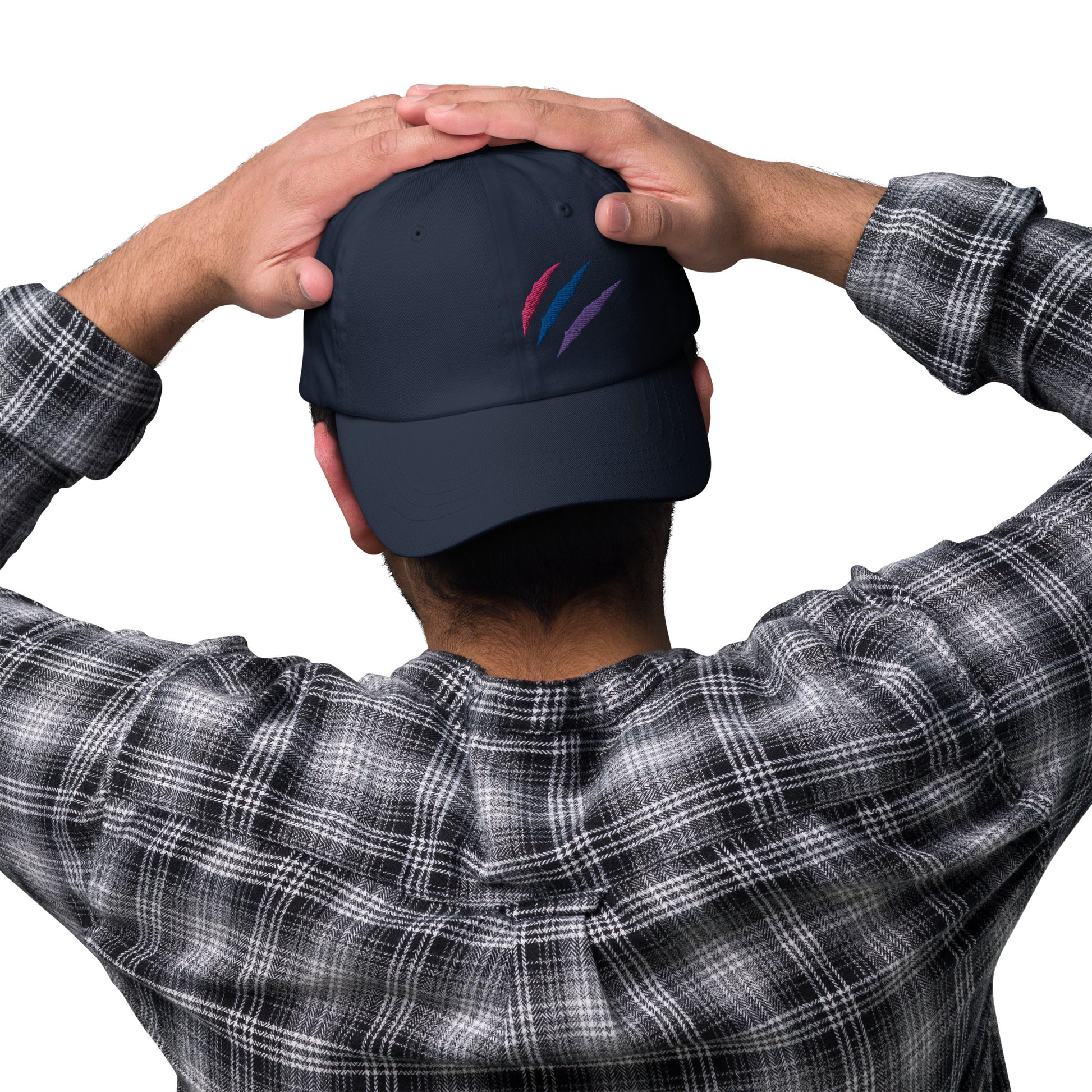 A male model wearing our baseball hat featuring bisexual pride scratch mark embroidery in navy with a low profile, adjustable strap.