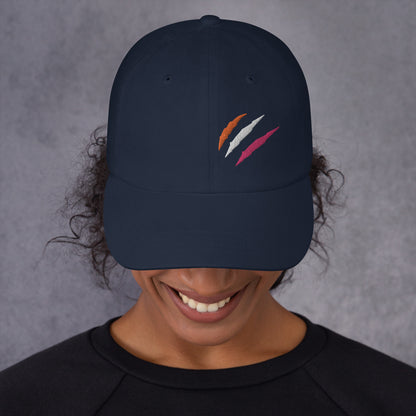 A female model wearing our navy baseball hat featuring lesbian pride scratch mark embroidery with a low profile, adjustable strap.