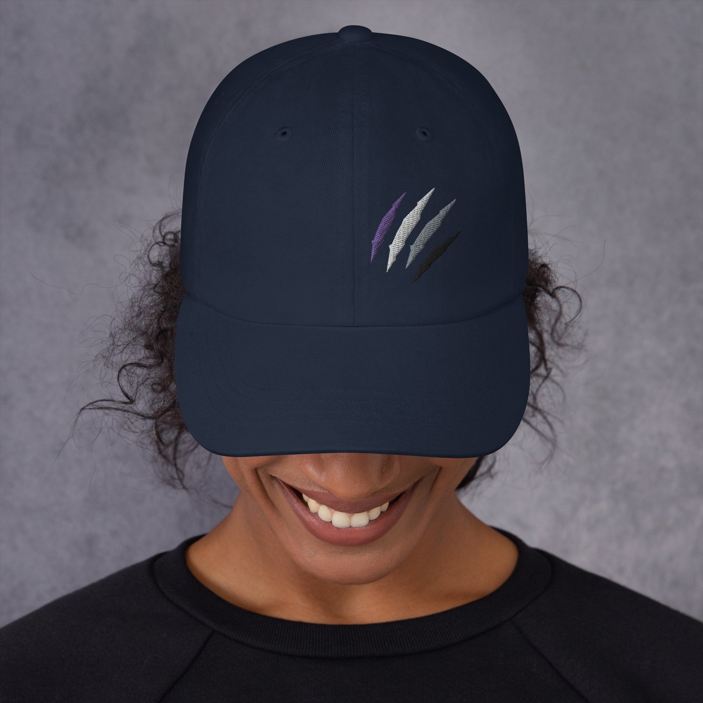 Female model wearing our baseball hat featuring asexual pride scratch mark embroidery in navy with a low profile, adjustable strap.