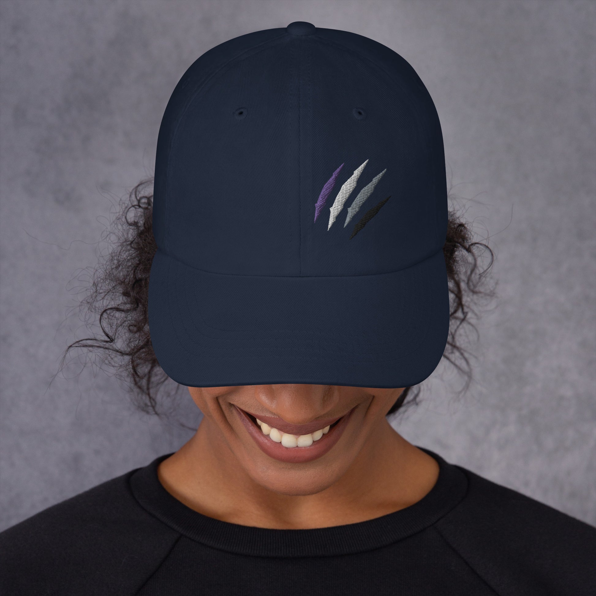 Female model wearing our baseball hat featuring asexual pride scratch mark embroidery in navy with a low profile, adjustable strap.