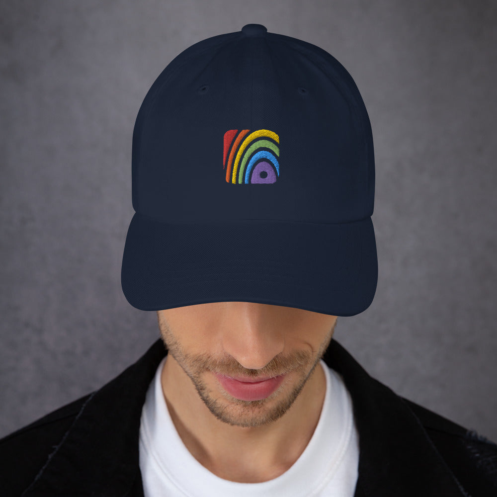A male model wearing our navy baseball hat featuring rainbow design embroidery with a low profile, adjustable strap.
