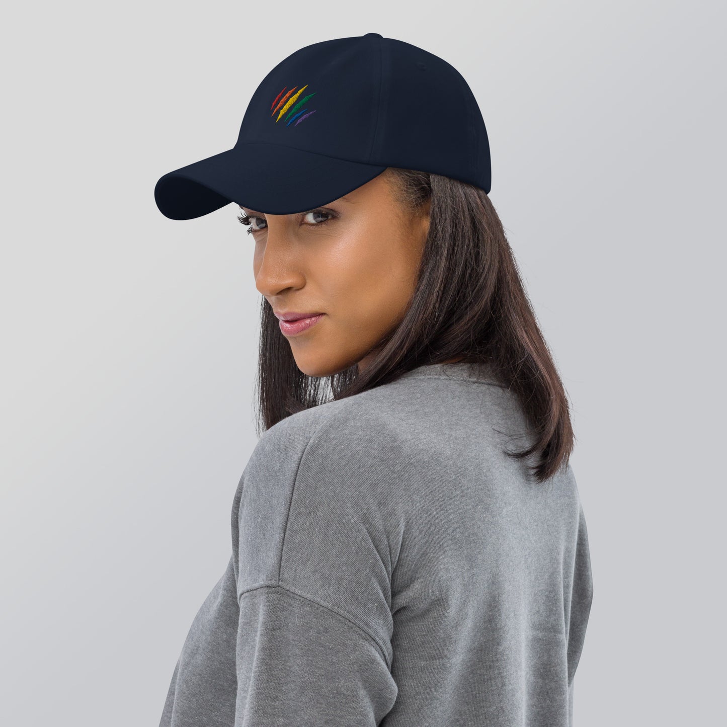 A model wearing our navy baseball hat featuring rainbow pride scratch mark embroidery with a low profile, adjustable strap.