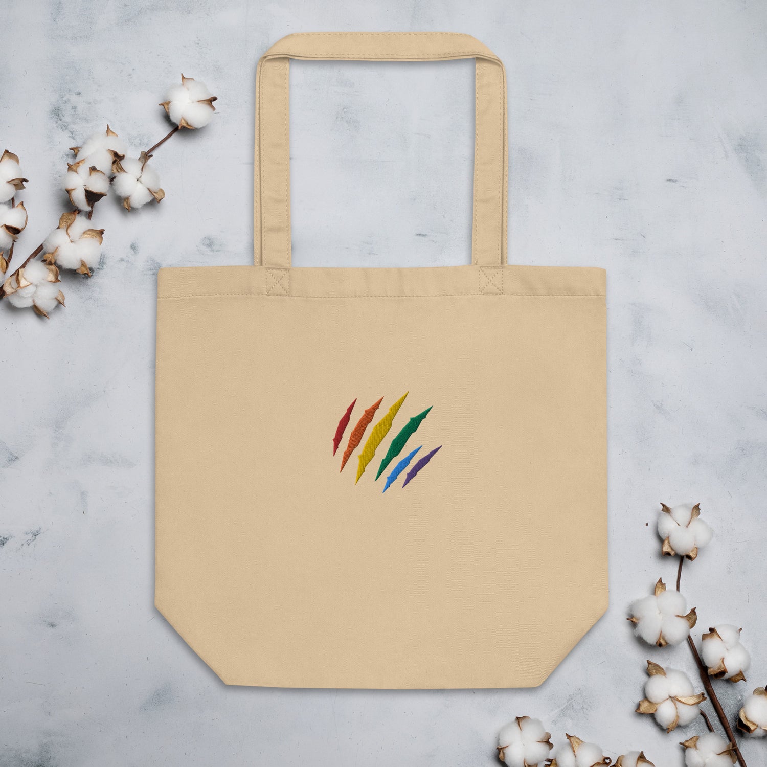 Eco Tote Bag in oyster color with an embroidered Rainbow Mark on the front, a nod to our LGBTQ+ community. 