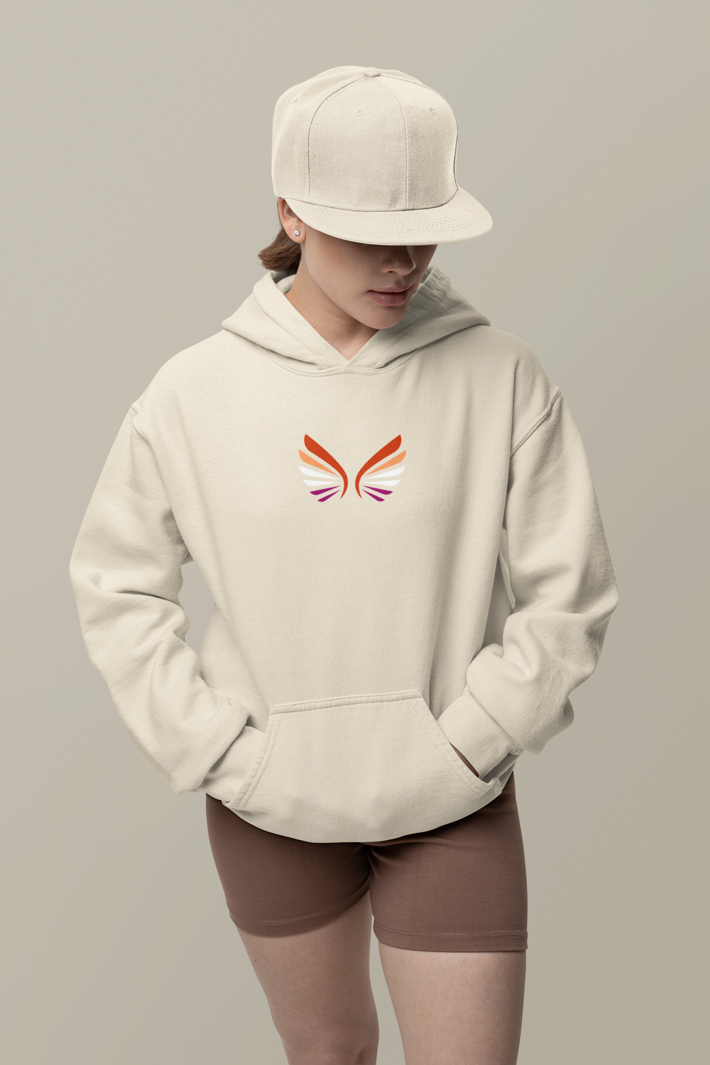 Female model wearing an organic cotton hoodie, featuring an embroidered wing design on the front centre in lesbian colors. 