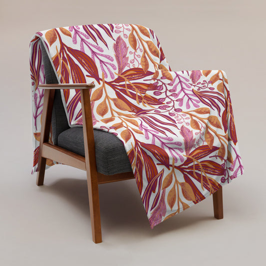 Soft throw blanket hanging over an armchair. Lesbian pride flag colors in a leafy garden style print