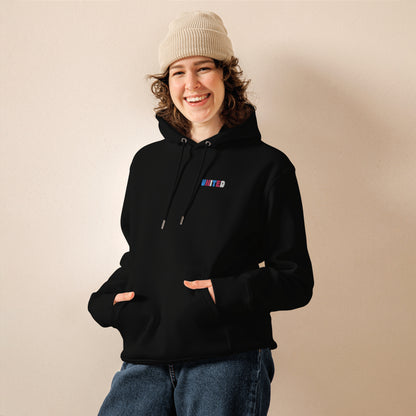 A female model wearing our unisex eco-friendly black hoodie featuring on the upper left chest; united embroidery in transgender pride colors, adding a touch of lgbtq to your outfit. sizes: small, medium, large, extra large, double extra large.