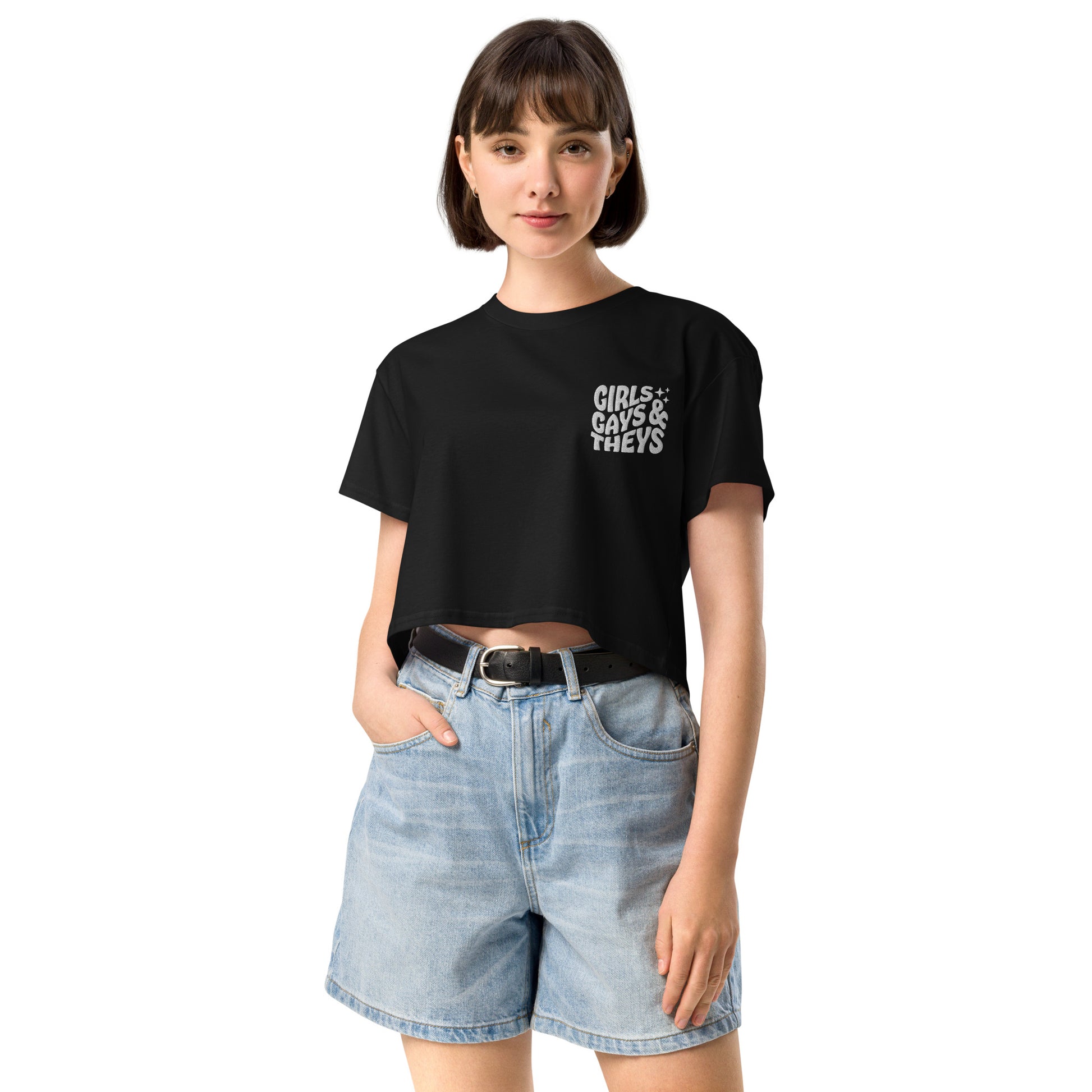A female model wearing a relaxed, modest black crop top features a subtle white embroidery featuring the quote: girls gays & they's. Adding a touch of LGBTQ+ to your look—a playful celebration of queer culture! Made from 100% combed cotton. Available in Extra Small, Small, Medium, Large, Extra Large.