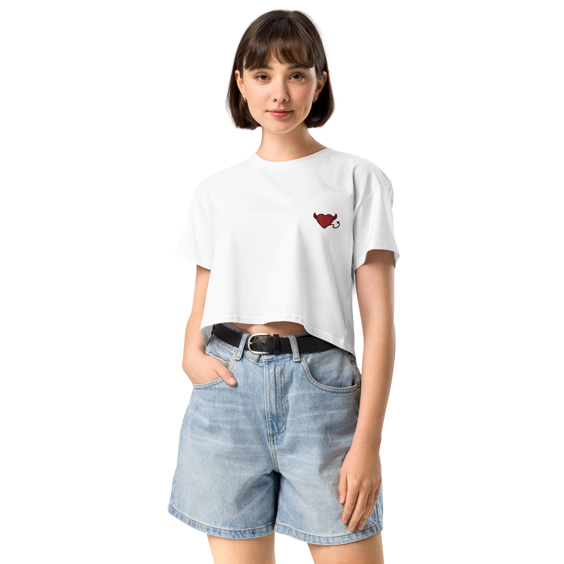 A female model wearing a relaxed, modest white crop top features a subtle red embroidery featuring a devil's heart. Adding a touch of mischief to your look—a playful celebration of lgbtq culture! Made from 100% combed cotton. Available in Extra Small, Small, Medium, Large, Extra Large.